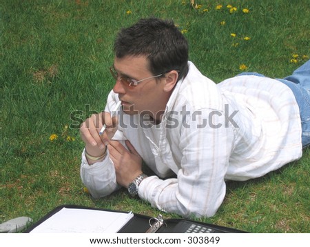 Young man working, doing homework, laying on the grass