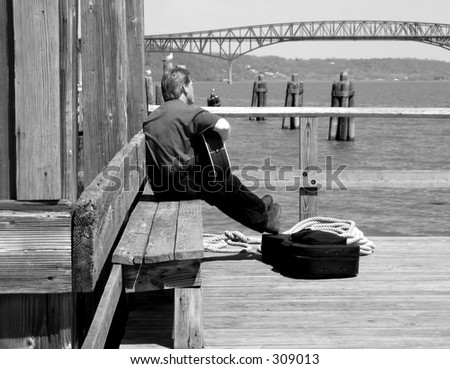 Musician strums his guitar while looking out over the Hudson River in New York; black and white