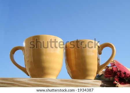 Two yellow mugs on porch against blue sky