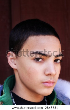 Portrait of multi-cultural teen boy with serious look against dark background