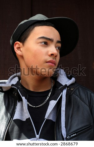 Portrait of multi-cultural teen boy wearing cap and leather jacket against dark textured background