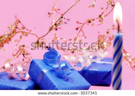 Birthday candle and blue gifts on pink with gold star decorations (focus on gift)