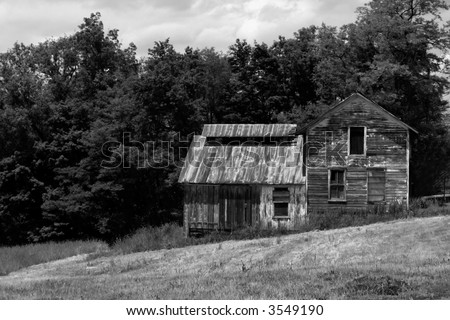 Abandoned farm house with chipped paint and boarded windows; black and white