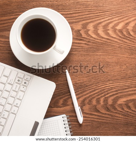 Office table with notepad, computer, pen and coffee cup