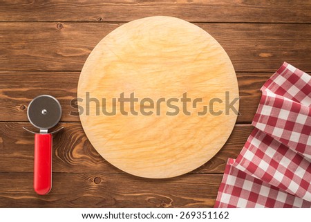 Pizza cutting board with tablecloth and round knife on wooden background
