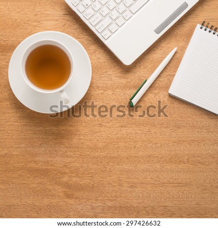 Computer, pen, notepad and tea cup on a table