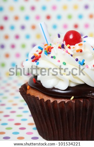 Birthday Cupcake with sprinkles and a cherry on a polka dot patterned background.