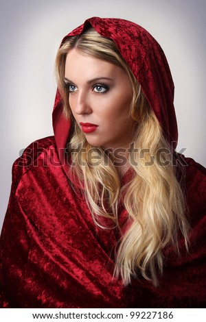 Portrait of a young attractive woman dressed as Little Red Riding Hood wearing a red cape.