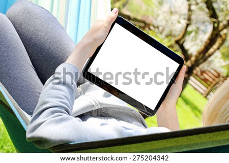 woman using digital tablet while relaxing in hammock at backyard