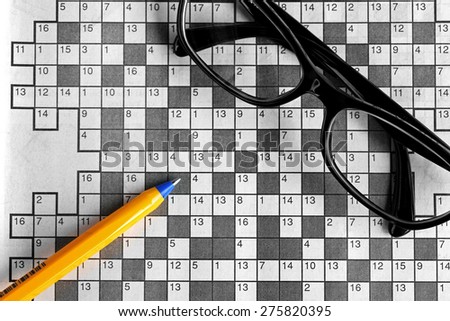 top view of blank crossword puzzle with black eyeglasses and a pen