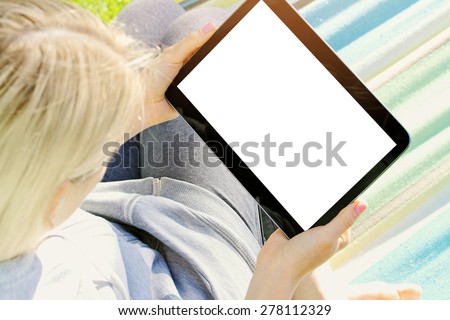 over the shoulder view of a woman relaxing in a hammock using a digital tablet