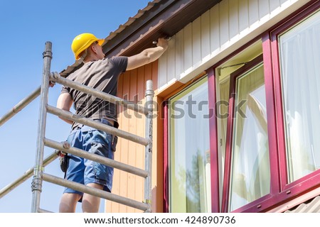 construction worker on scaffolding painting wooden house facade