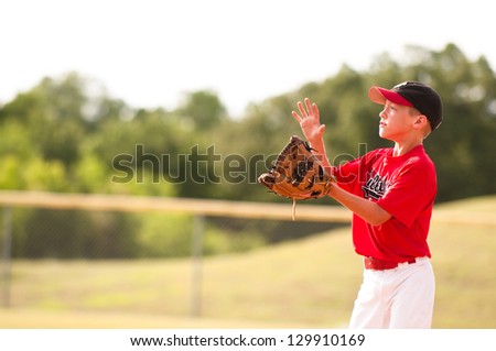 Young baseball player in red jersey about to catch the pop fly.