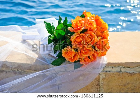 Beautiful wedding bouquet of orange flowers resting on the Brides Veil, next to a swimming pool of blue water.
