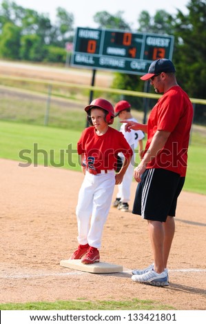 Baseball coach giving instruction to player at first base during a game.