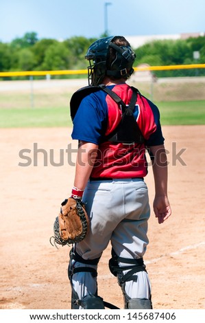 A teen boy baseball catcher from behind, standing during a game.