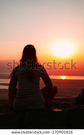 Silhouetted woman sitting on the ground and looking to the sunset
