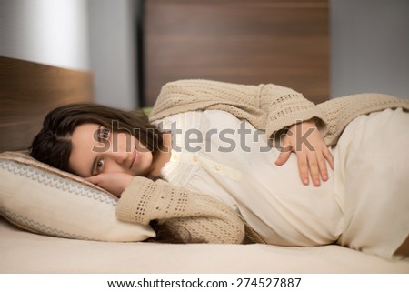 Pregnant woman in home clothes laying on the pillow in the bedroom with modern furniture