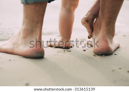 Bare feet father and his little son staying in the sand near the water