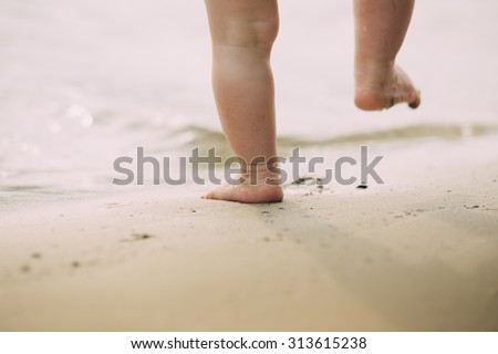 Toddler baby doing his first steps on the sand near the bank