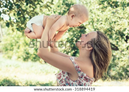 Happy mother playing with her toddler sun. Mother and baby laughing to each other. Child in the mother hands. Outdoor portrait.