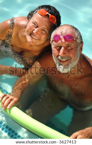 Happy retired couple having fun in the swimming pool in bright matching goggles