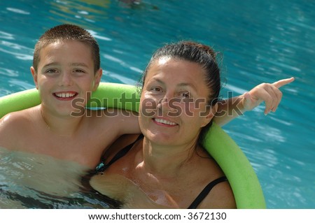 Gorgeous grandmother and her cute grandson swimming along in their pool