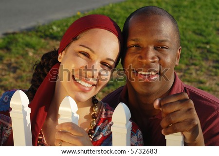 Newlywed couple holding on to a white picket fence, full of dreams and hopes for the life ahead