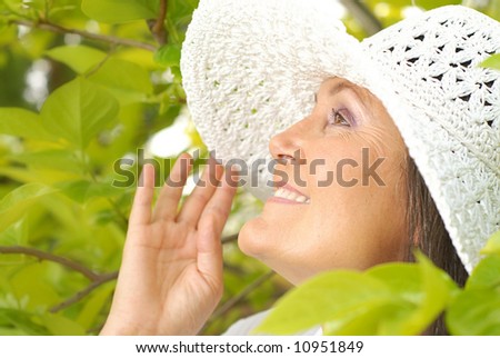 Older woman in a summer hat smiling outside among green leaves