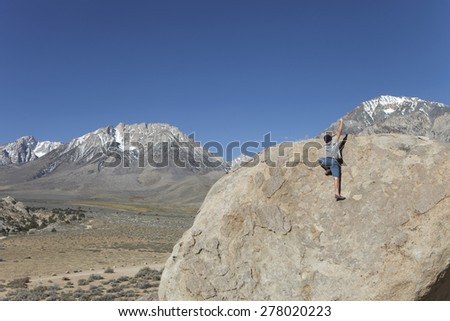 Man tops out on a boulder in the Buttermilks outside of Bishop, CA