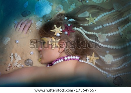 Pretty girl with pearls and shells in her hair is lying on the sand