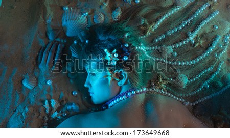 Pretty girl with pearls and shells in her hair is lying on the sand