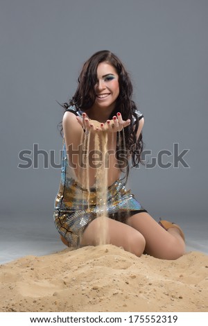 Cute girl in a very beautiful dress thinking about life and money which run so fast like the sand flowing through her fingers