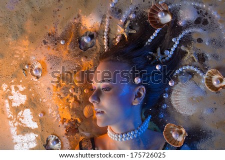 Beautiful girl with fantastic hair full of pearls and shells is lying on the sand