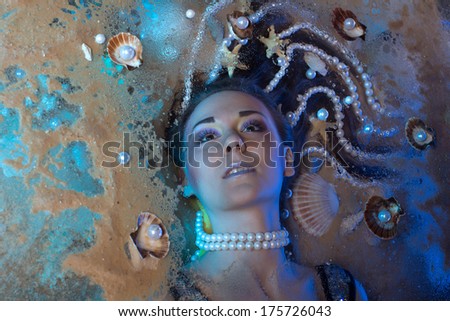 Beautiful girl with fantastic hair full of pearls and shells is lying on the sand