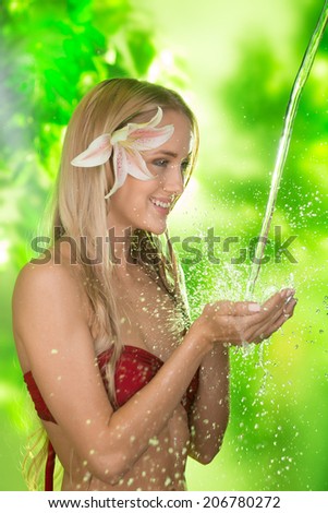 Attractive young girl with a summer flower in her hair catching splashes of fresh cold water with her hands