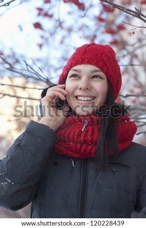 the young girl in a red knitted cap and a red scarf speaks by phone on the winter street