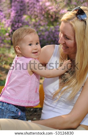 The little girl with mum sit in a garden on a bench in the afternoon