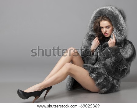 The young beautiful girl in a fur coat sits on a floor
