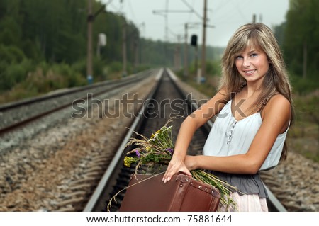 The young beautiful girl the blonde costs at railway station with a suitcase and a bouquet of wild flowers