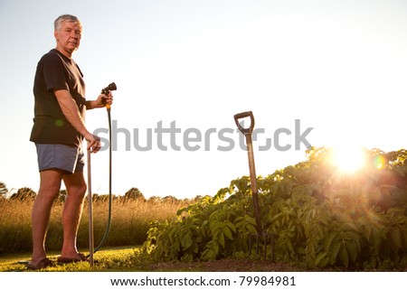 Mature man spraying water with a garden hose.