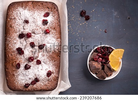 Chocolate and cranberry cake with dried berries and chocolate on dark wooden table rustic still life