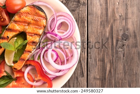 Grilled salmon steak with sliced onion and tomatoes on old wooden table top view at left side