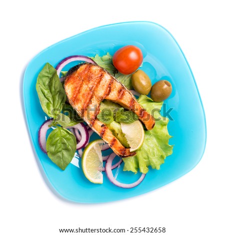 Grilled salmon steak with sliced onion and tomatoes on blue plate isolated on white top view