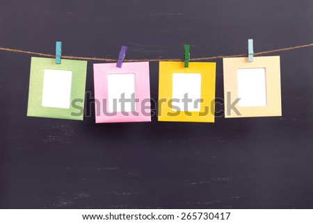 Four colored paper photo frames hanging on rope on gray background