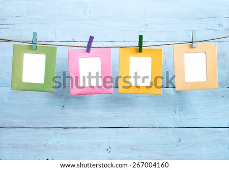 Four colored paper photo frames hanging on rope on blue painted background