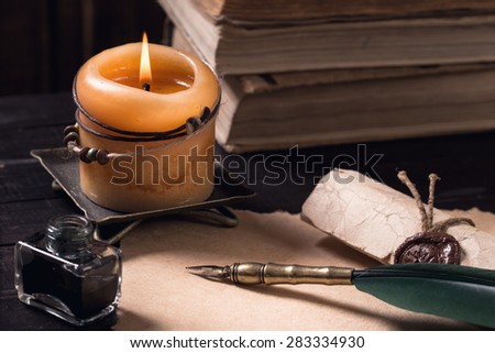 Letter, quill pen with lighted candle and pile of old books on dark background still-life