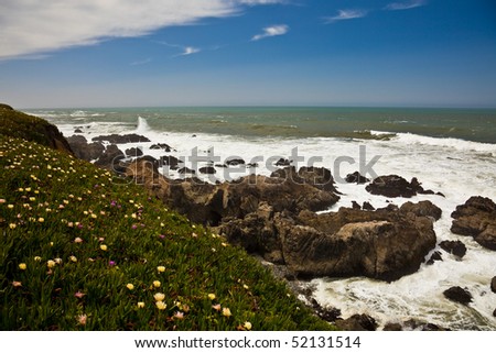 Scenic view of waves breading on rocky ocean coastline under blue skies and clouds.