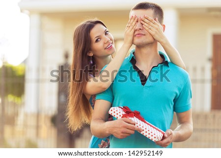 woman covering man\'s eyes hands. man with gift