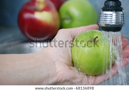 A Hand Washing a Delicious Green Granny Smith Apple in a Sink with More Apples in the Background